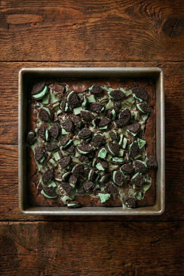 Fudgy chocolate brownies are filled with layers of Mint Oreos and Andes Mints to create these epic Andes Mint Brownies. A square baking pan filled with brownies topped with melted andes mints and chopped mint Oreo cookies.