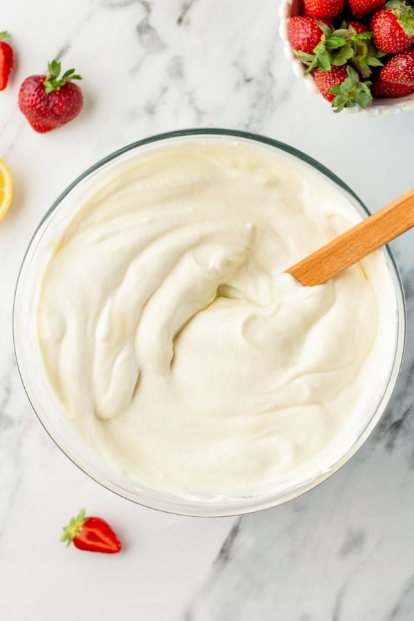 With no ice cream maker needed, this velvety Strawberry Cheesecake Ice Cream recipe has thick swirls of strawberry compote and graham cracker crumbs. A glass bowl filled with a creamy no-churn ice cream mixture sits on a marble surface, with a wooden spatula inside.