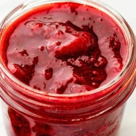 A glass mason jar filled with homemade strawberry compote sits on a white surface.