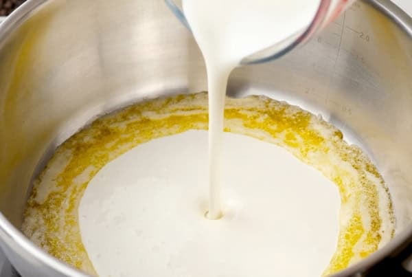 Thick, creamy, homemade Alfredo sauce recipe in 10 minutes with just 5 ingredients and a pinch of nutmeg, the Italian secret most home cooks skip! Cream is being poured from a glass measuring cup into a stainless steel pot containing melted butter, starting to mix together.