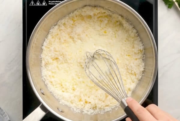 Thick, creamy, homemade Alfredo sauce recipe in 10 minutes with just 5 ingredients and a pinch of nutmeg, the Italian secret most home cooks skip! A hand whisking grated parmesan cheese into a creamy white sauce in a stainless steel pan on a stovetop.