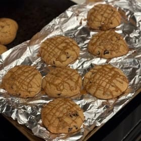 Large Biscoff stuffed cookies on a foil-lined baking sheet, topped with a crisscross drizzle of cookie butter.