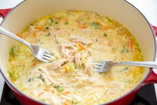 The best homemade Chicken and Dumplings recipe you'll ever make! Ready in under an hour with a thick creamy broth, juicy chicken, and big fluffy dumplings. A pot of creamy chicken soup with shredded chicken, carrots, celery, and herbs. Two forks are pulling pieces of chicken apart in the center of the soup.