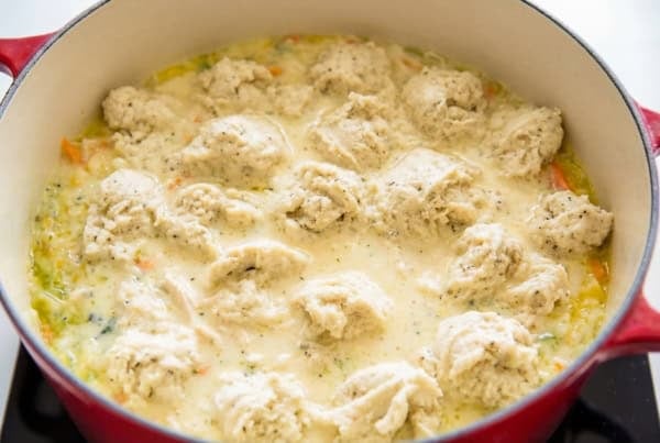 The best homemade Chicken and Dumplings recipe you'll ever make! Ready in under an hour with a thick creamy broth, juicy chicken, and big fluffy dumplings. A red pot filled with a creamy chicken soup mixture, topped with raw dumpling dough dropped in spoonfuls.