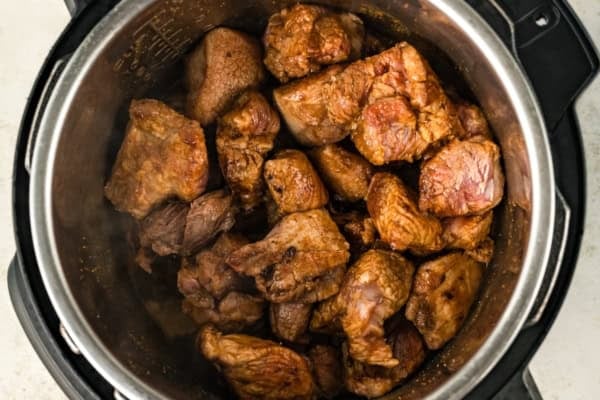 Fall-apart tender Instant Pot pulled pork recipe with a smoky brown sugar rub and tangy BBQ sauce. Done in 90 minutes, no smoker required! Large chunks of browned pork are searing in an Instant Pot, with steam rising and the sides of the metal pot visible.