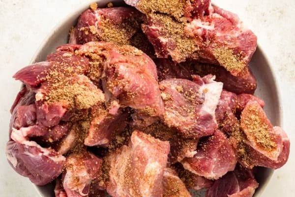 Fall-apart tender Instant Pot pulled pork recipe with a smoky brown sugar rub and tangy BBQ sauce. Done in 90 minutes, no smoker required! A bowl filled with raw chunks of pork that are generously coated with a spice rub.