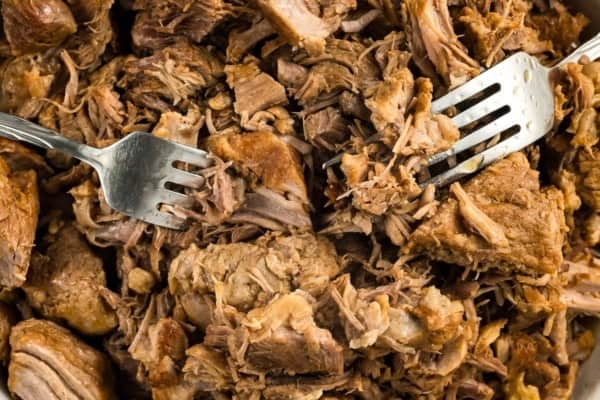 Fall-apart tender Instant Pot pulled pork recipe with a smoky brown sugar rub and tangy BBQ sauce. Done in 90 minutes, no smoker required! Two metal forks shredding cooked, tender, brown pulled pork into pieces.