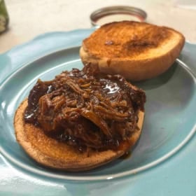A toasted sandwich bun on a light blue plate, topped with a generous serving of saucy shredded pulled pork made in the instant pot.