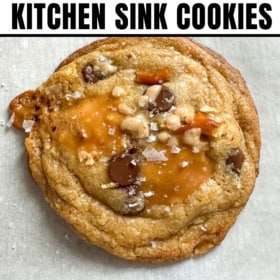 A close-up of brown butter kitchen sink cookies with caramel, chocolate chips, and sea salt on parchment paper.