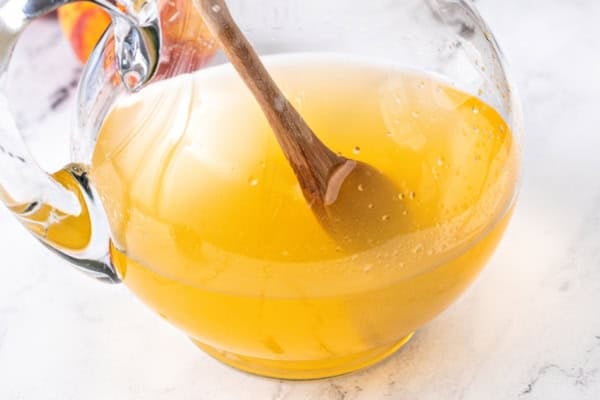 White Peach Sangria recipe is made with crisp white wine, peach nectar, schnapps and fresh fruit. The easiest summer cocktail you'll make all season! A clear glass pitcher filled with peach and white wine sangria being stirred with a wooden spoon.