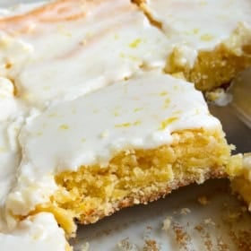 Close-up of frosted lemon blondies cut into squares on a baking tray, with one square slightly pulled out to show the moist, yellow interior.