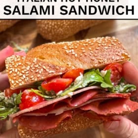 A hand holds a Hot Honey Salami Sandwich filled with salami, arugula, tomato, and cheese.