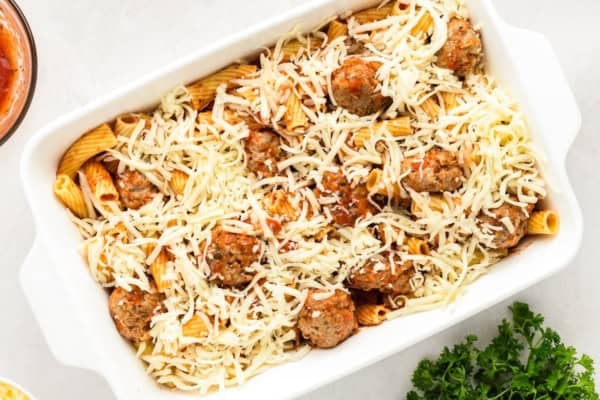 With seared meatballs, lots of cheese, and perfectly cooked saucy pasta (that's never mushy), this is the best Meatball Casserole recipe! A white casserole dish filled with rigatoni pasta, meatballs, tomato sauce, and topped with shredded cheese, ready to be baked.