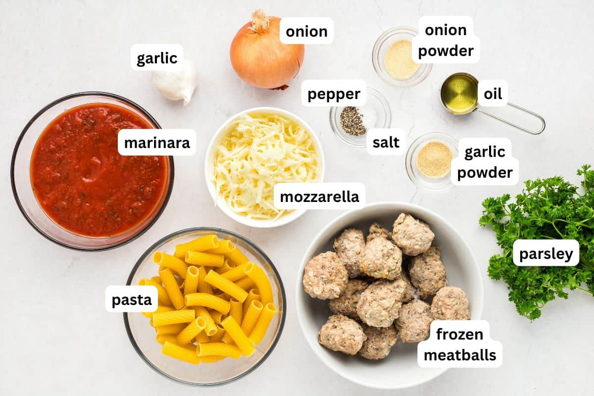 With seared meatballs, lots of cheese, and perfectly cooked saucy pasta (that's never mushy), this is the best Meatball Casserole recipe! Labeled ingredients for a meatball casserole recipe arranged on a white surface, including garlic, onion, marinara sauce, mozzarella cheese, pasta, frozen meatballs, parsley, oil, pepper, salt, onion powder, and garlic powder.