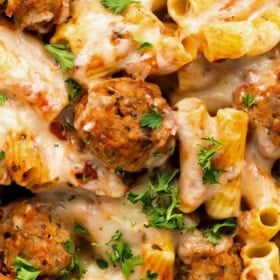 Close-up of cheesy baked pasta casserole with meatballs, rigatoni, melted mozzarella, tomato sauce, and parsley.