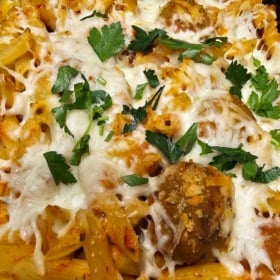 Close-up of baked ziti with meatballs, melted cheese, and tomato sauce, topped with fresh chopped parsley.