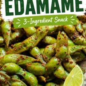 A close-up of chili lime edamame snack garnished with lime wedges.