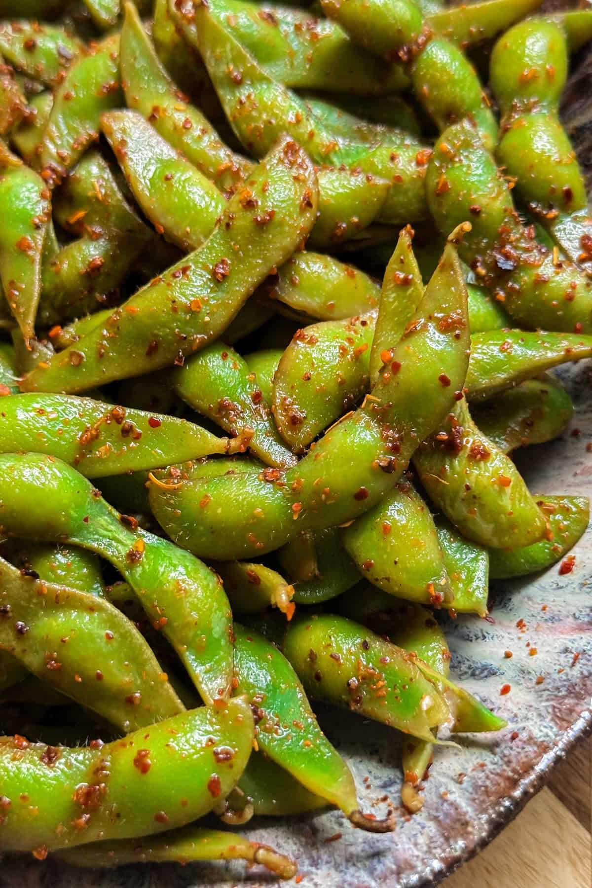 Make the BEST spicy edamame recipe at home with frozen pods, fresh lime, and Tajin. Easy, addictive, and ready in just 5 minutes! A close-up of a plate filled with bright green spicy edamame pods coated in lime juice and chili seasoning.