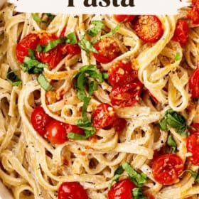 A bowl of fettuccine pasta with roasted cherry tomatoes and fresh basil, coated in a creamy sauce. Text on image reads: Roasted Cherry Tomato Pasta.