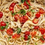 A bowl of creamy tomato pasta topped with roasted cherry tomatoes and fresh basil, garnished with herbs.