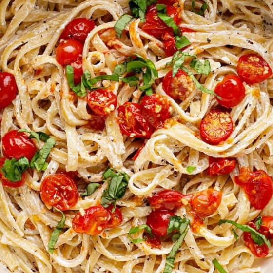 A bowl of creamy tomato pasta topped with roasted cherry tomatoes and fresh basil, garnished with herbs.