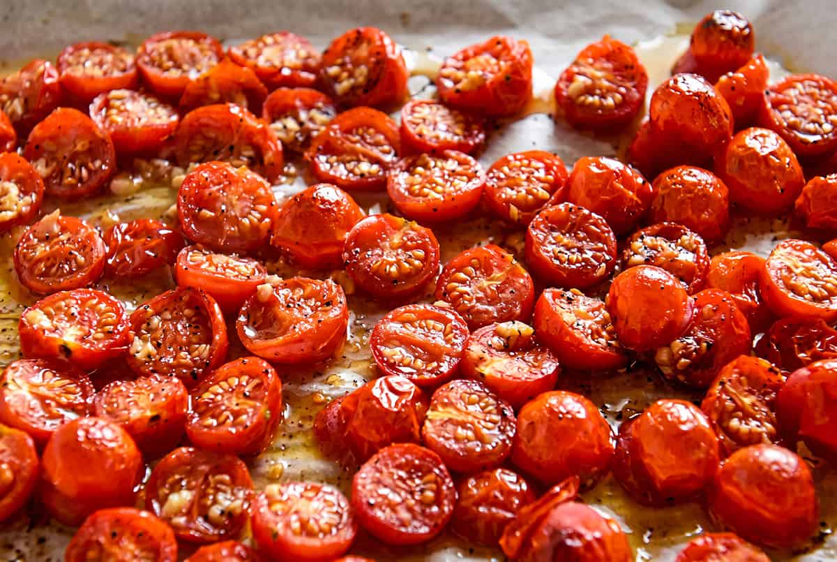 This creamy Cherry Tomato Pasta recipe is loaded with garlic roasted tomatoes and a tangy goat cheese sauce. An easy dinner ready in 30 minutes! Halved roasted cherry tomatoes, seasoned and glistening, lay on a parchment-lined baking sheet.