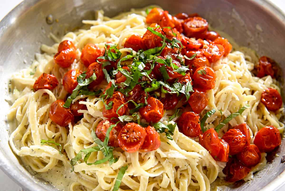 This creamy Cherry Tomato Pasta recipe is loaded with garlic roasted tomatoes and a tangy goat cheese sauce. An easy dinner ready in 30 minutes! A bowl of creamy tomato pasta topped with roasted cherry tomatoes and fresh sliced basil, served in a metal dish.
