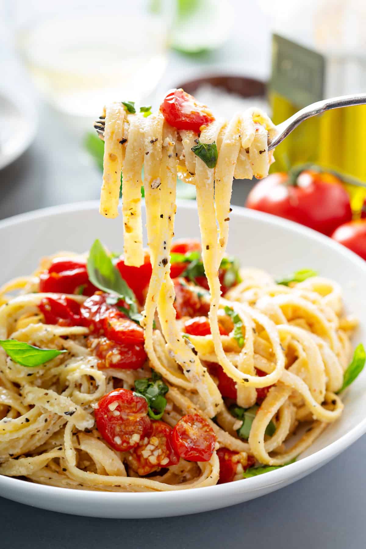 This creamy Cherry Tomato Pasta recipe is loaded with garlic roasted tomatoes and a tangy goat cheese sauce. An easy dinner ready in 30 minutes! A fork lifts creamy tomato pasta with roasted cherry tomatoes, basil, and black pepper from a white bowl.