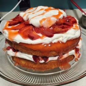 Two-layer strawberry whipped cream cake with sliced strawberries and whipped cream between layers on a glass plate.
