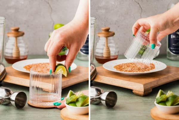 A hand rubs a lime wedge on a glass rim, then dips the rim into a plate of Tajin seasoning on a wooden board, preparing a spiced drink glass.