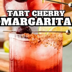 A glass of tart cherry margarita with ice, chili rim, lime wedges, and cherries on a cocktail pick. Text overlay reads “Tart Cherry Margarita.”.