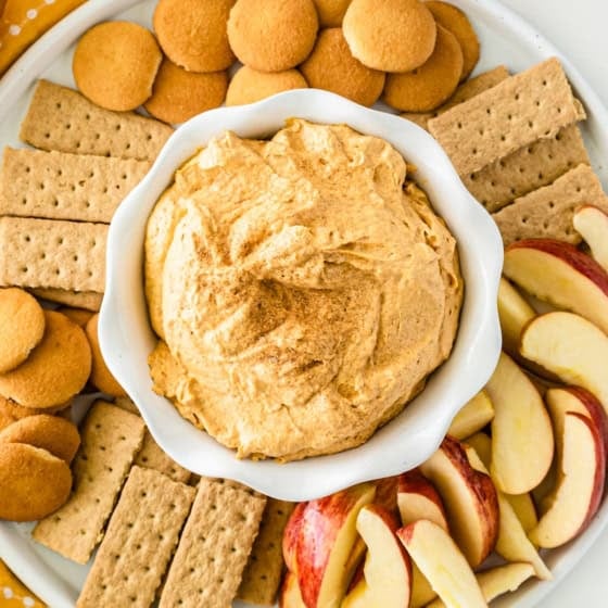 A plate with sweet potato pie dip in a bowl at the center, surrounded by vanilla wafers, graham crackers, and sliced apples, arranged neatly for dipping.