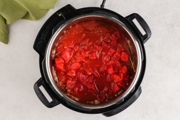 This hearty Instant Pot Spaghetti tastes like it simmered all afternoon, but it's ready in just 30 minutes and made in one single pot. An overhead view of a pressure cooker filled with tomato sauce and diced tomatoes, sitting on a light countertop with a green cloth nearby.