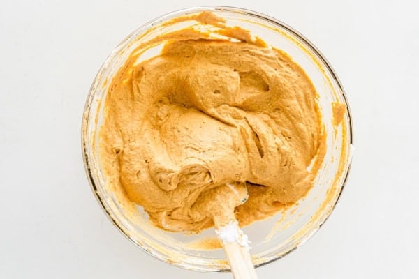 This Sweet Potato Pie Dip tastes like a classic sweet potato pie, but in a scoopable form. Serve it with gingersnaps or graham crackers! A glass bowl filled with creamy sweet potato dip, with a wooden spatula partially submerged, sits on a white surface.