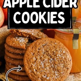 A stack of apple cider cookies with sugar on top, next to a jar of apple cider and fresh apples.