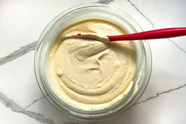Pumpkin Pie Pudding layers a whole pumpkin pie with buttery graham crackers and the fluffiest pudding into the creamiest no-bake dessert! A glass bowl filled with smooth vanilla pudding and whipped cream mixture being mixed with a red spatula.