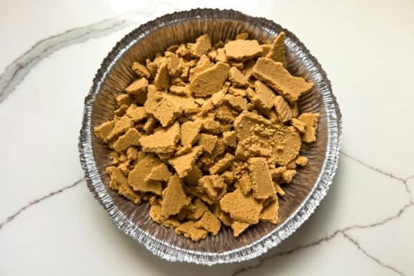 Pumpkin Pie Pudding layers a whole pumpkin pie with buttery graham crackers and the fluffiest pudding into the creamiest no-bake dessert! Two crumbled graham cracker pie crusts in a foil pie tin.