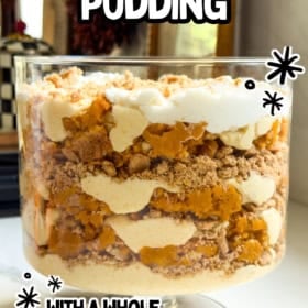 A pumpkin pie pudding trifle dish layered with crushed cookies, pumpkin pie filling, and whipped cream sits on a kitchen counter.
