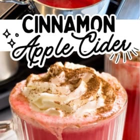 A glass mug filled with red hot cinnamon apple cider, topped with whipped cream and a dusting of cinnamon, with a pot of the cider simmering in the background.